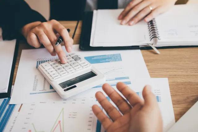 Two colleagues go through printed financial charts with a calculator and a notebook.