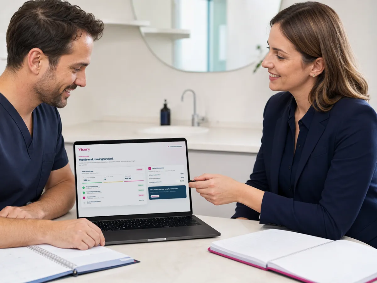 A clinician in scrubs and an advisor review the month-end close on a laptop at a clinic table.