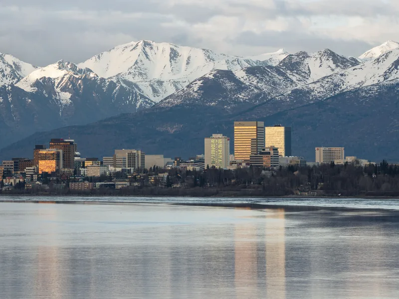 Anchorage’s downtown skyline across the water from Airport Park, with the snow-capped Chugach Mountains behind.