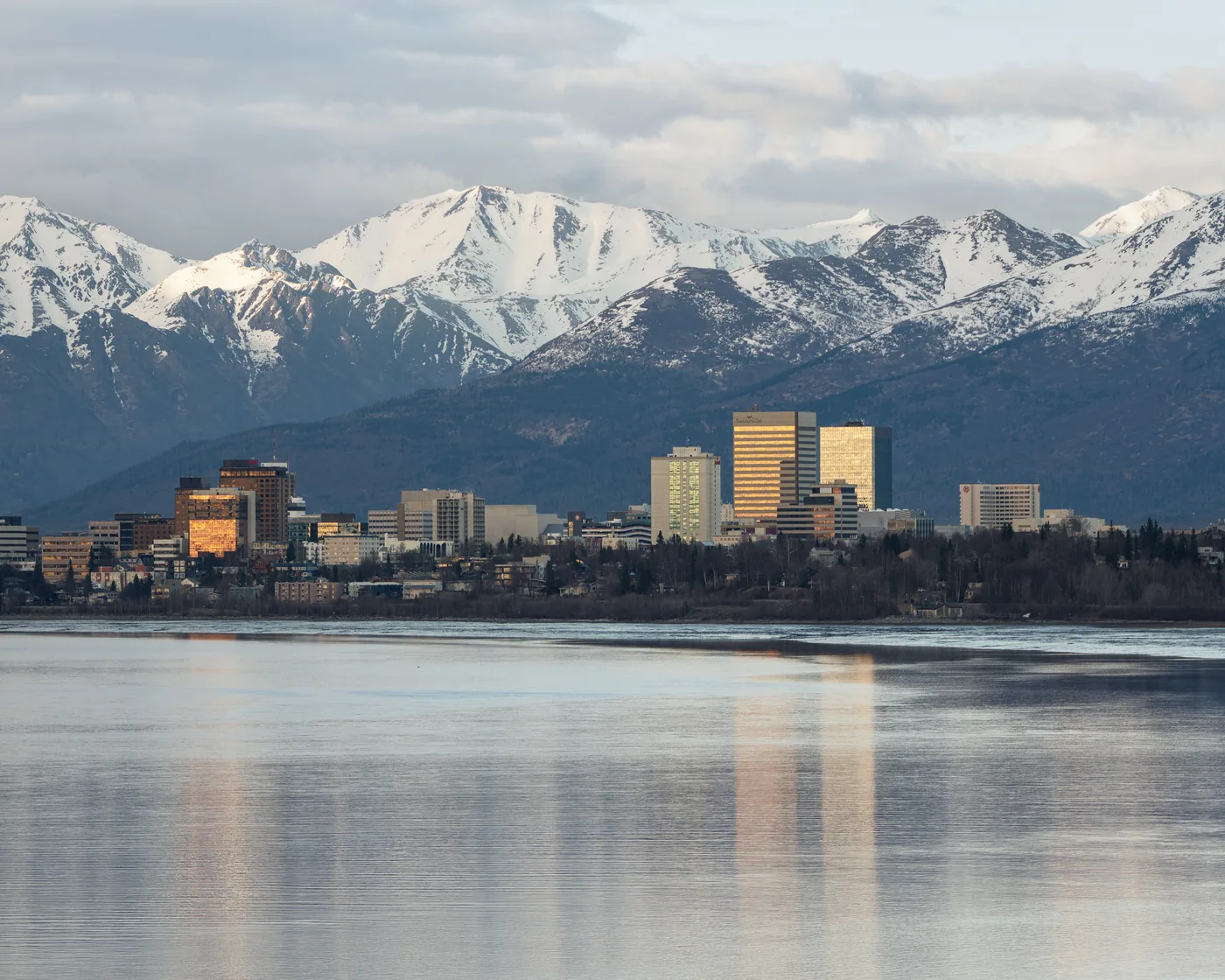 Anchorage’s downtown skyline across the water from Airport Park, with the snow-capped Chugach Mountains behind.