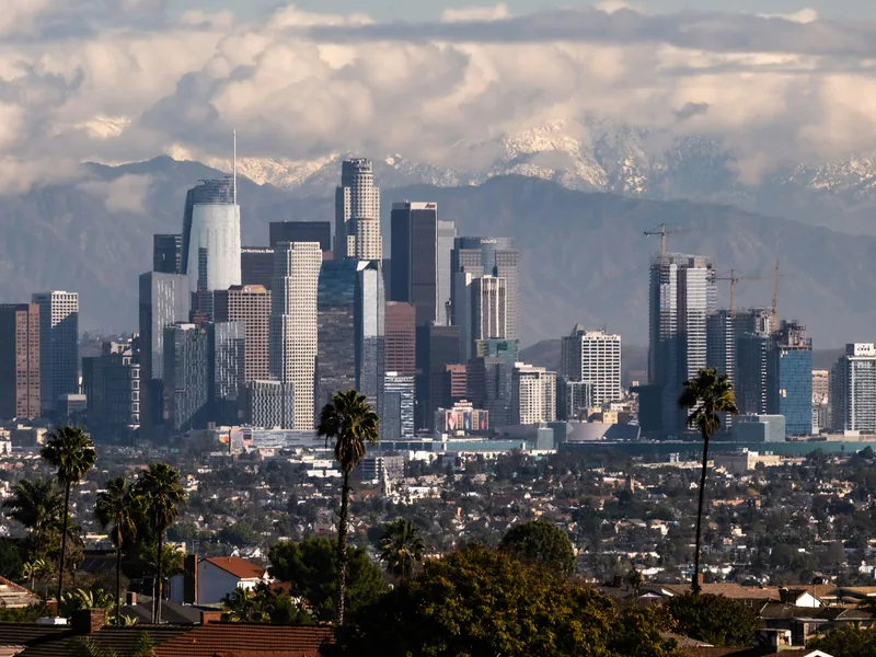 Palm trees in front of the downtown Los Angeles skyline, with snow on the mountains behind.