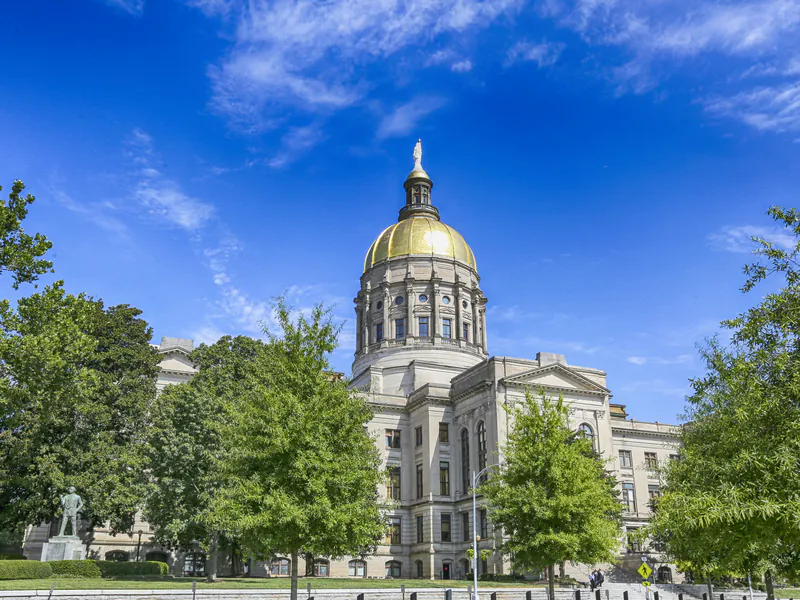 The gold dome of the Georgia State Capitol in Atlanta rising above green trees under a blue sky.