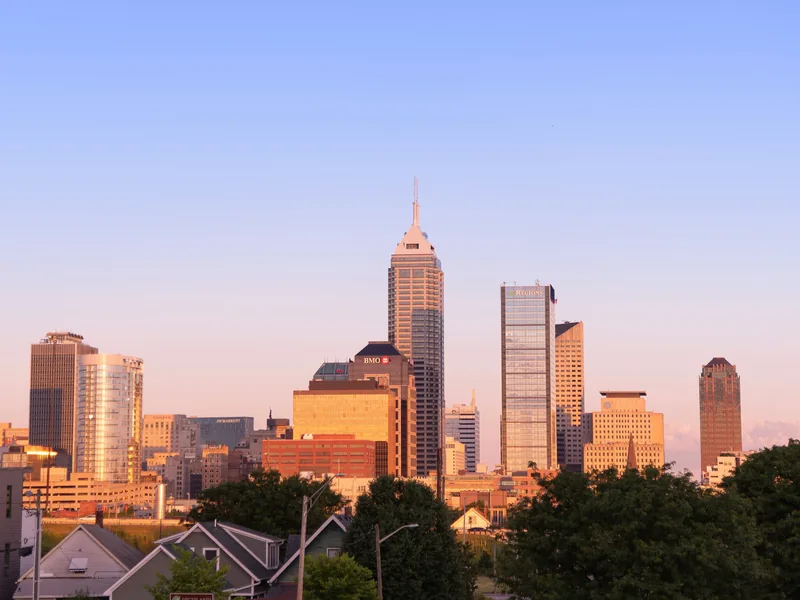 The Indianapolis skyline glowing in evening light above rooftops and trees.