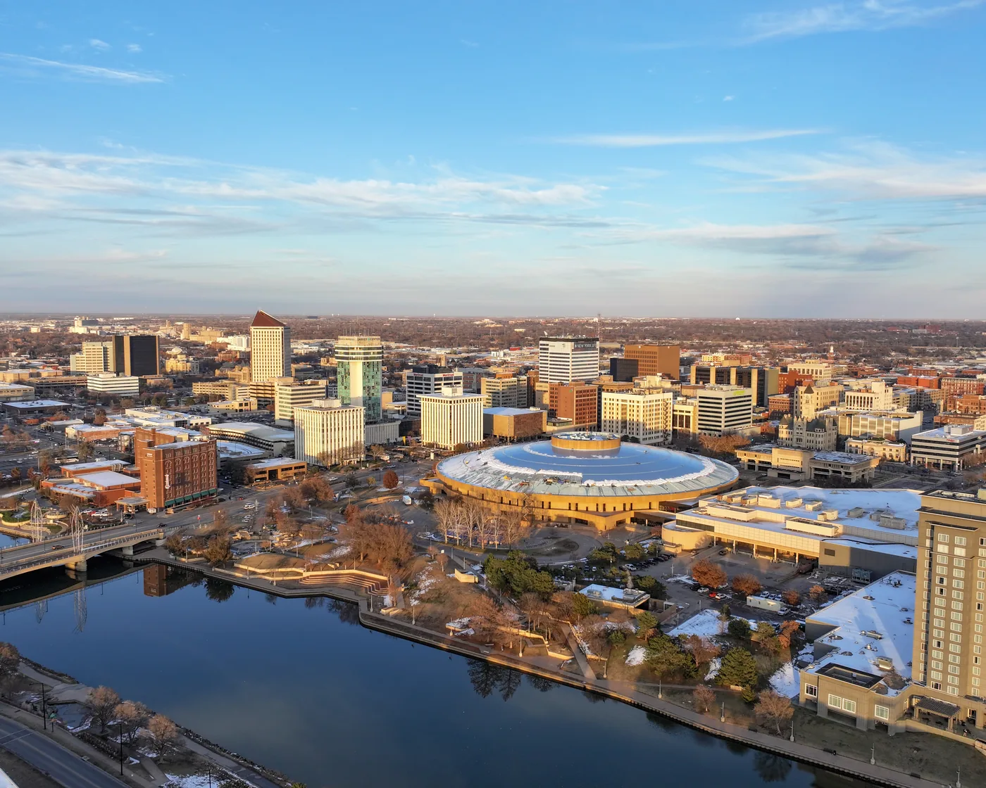 Downtown Wichita in late-afternoon light, with the round Century II hall beside the Arkansas River.