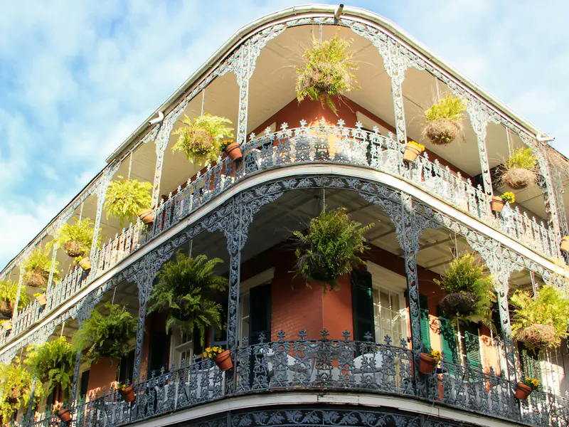 Cast-iron galleries hung with ferns wrap the corner of a red-brick building in the French Quarter of New Orleans.