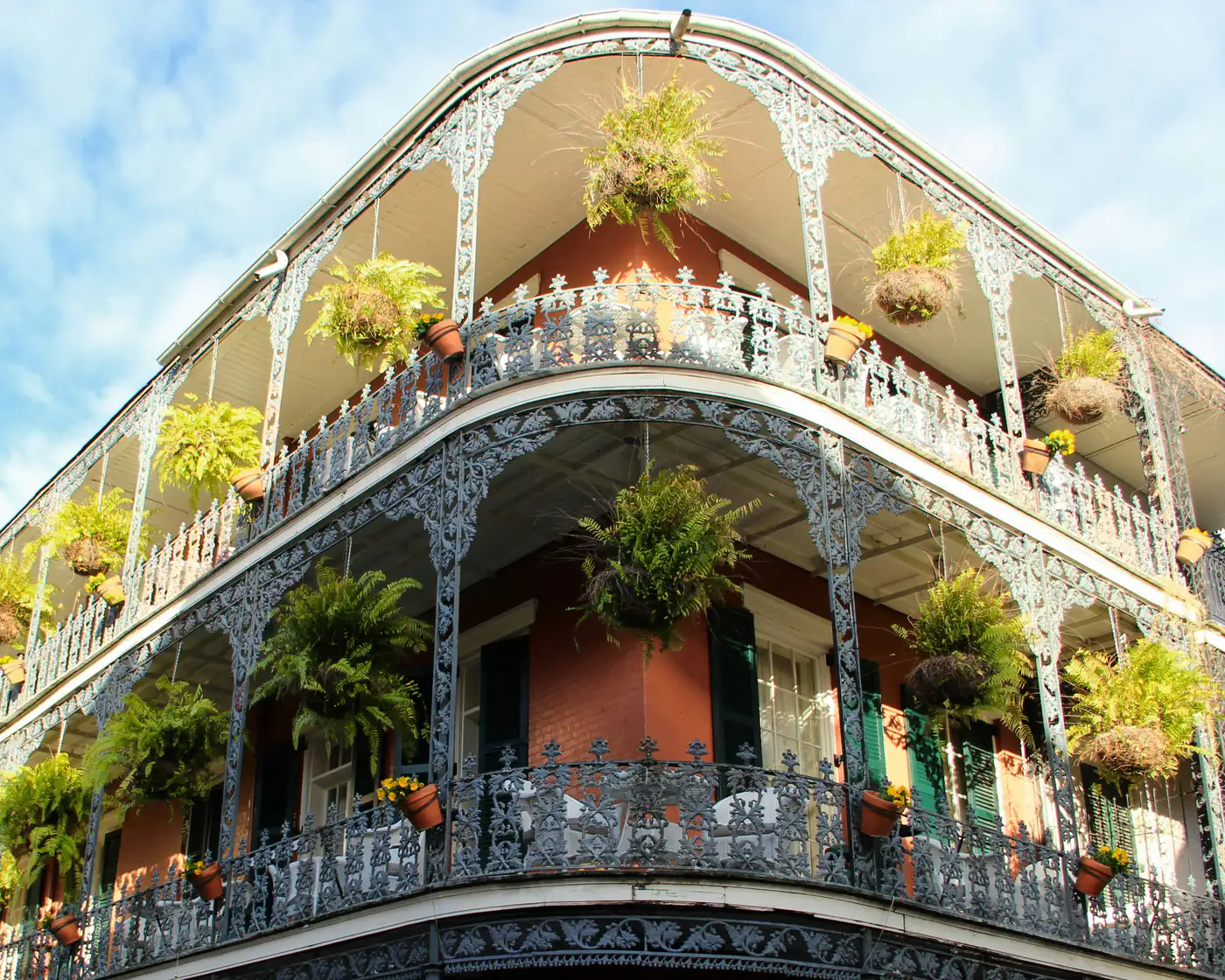 Cast-iron galleries hung with ferns wrap the corner of a red-brick building in the French Quarter of New Orleans.