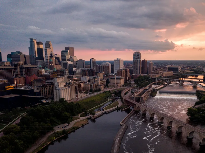 Downtown Minneapolis, the Stone Arch Bridge and St. Anthony Falls on the Mississippi River under a sunset sky.