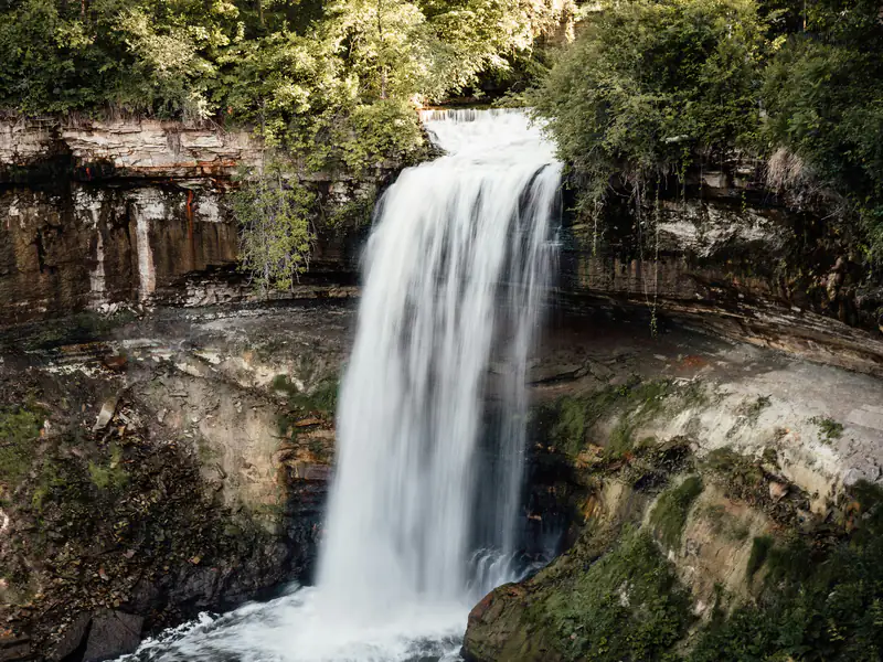 Minnehaha Falls in Minneapolis pouring over a limestone ledge into a wooded gorge.