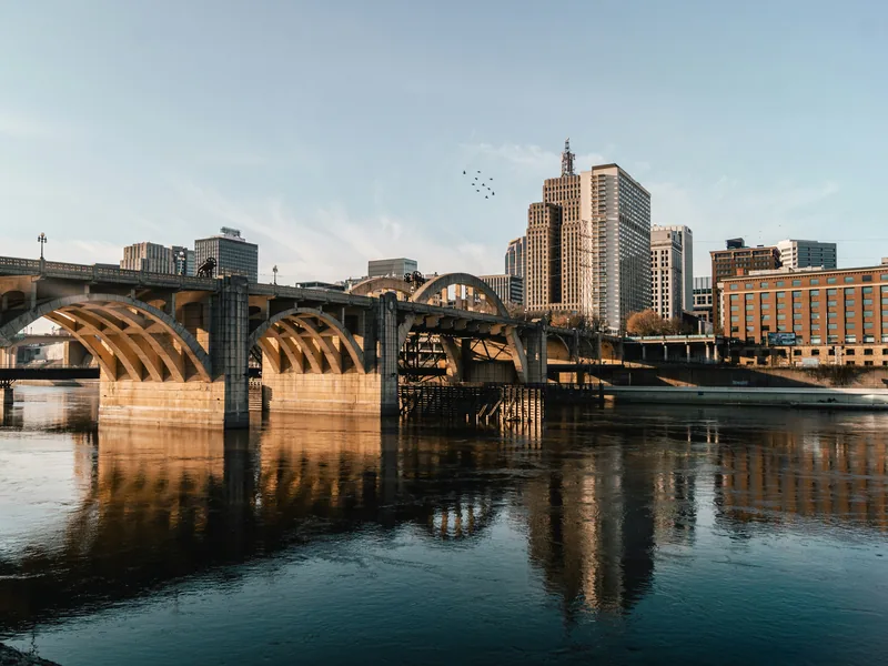 Downtown Saint Paul and the arches of the Robert Street Bridge reflected in the Mississippi River in warm light.