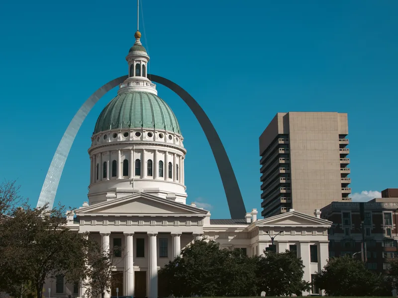 The Old Courthouse in downtown St. Louis, with the Gateway Arch rising behind its dome under a clear blue sky.