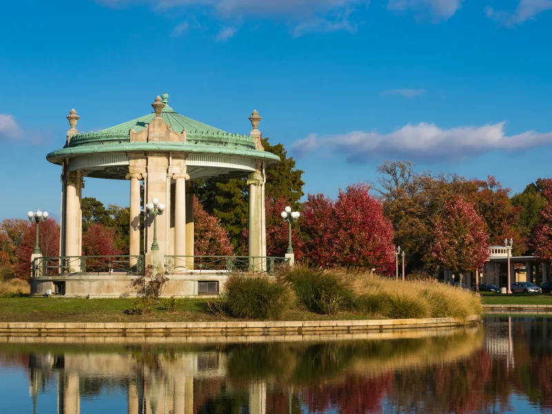 The Nathan Frank Bandstand on its island in Forest Park, St. Louis, among red autumn trees reflected in the lake.