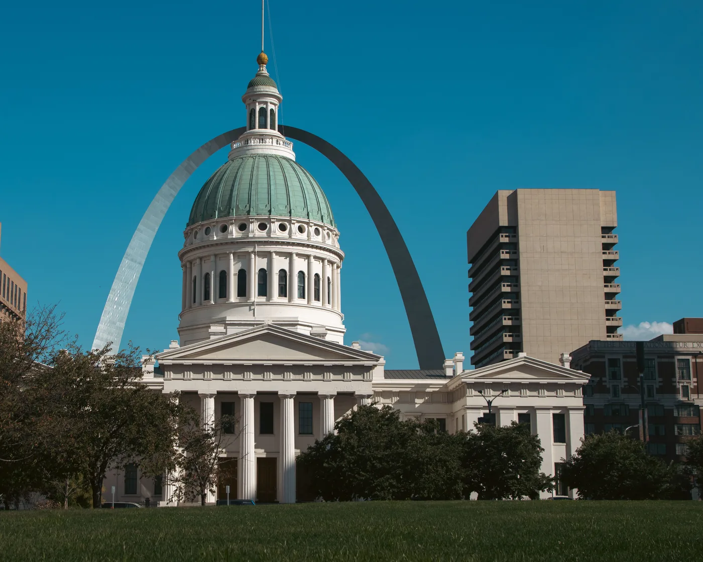 The Old Courthouse in downtown St. Louis, with the Gateway Arch rising behind its dome under a clear blue sky.