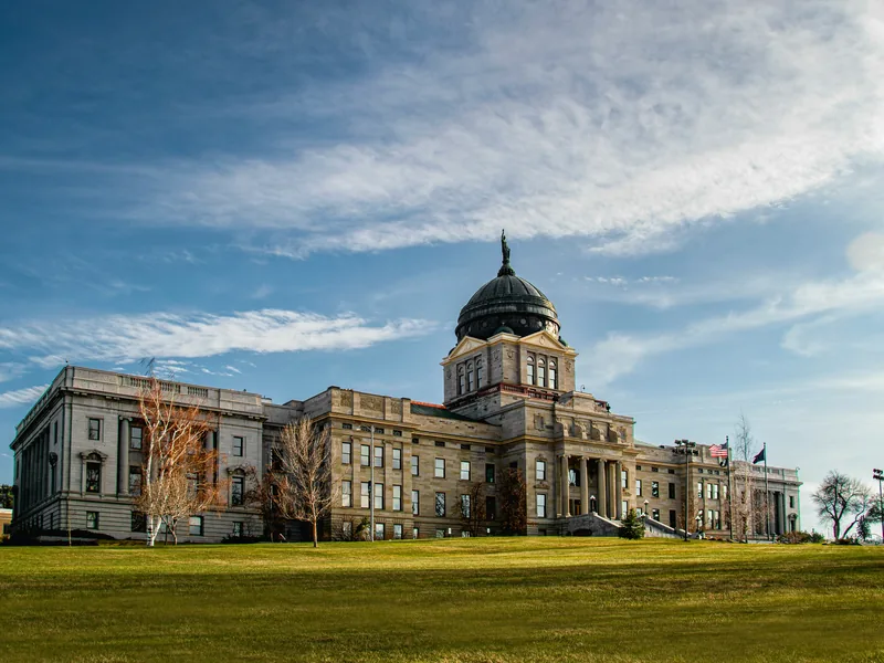The Montana State Capitol in Helena, with its copper dome, above a green lawn in afternoon light.