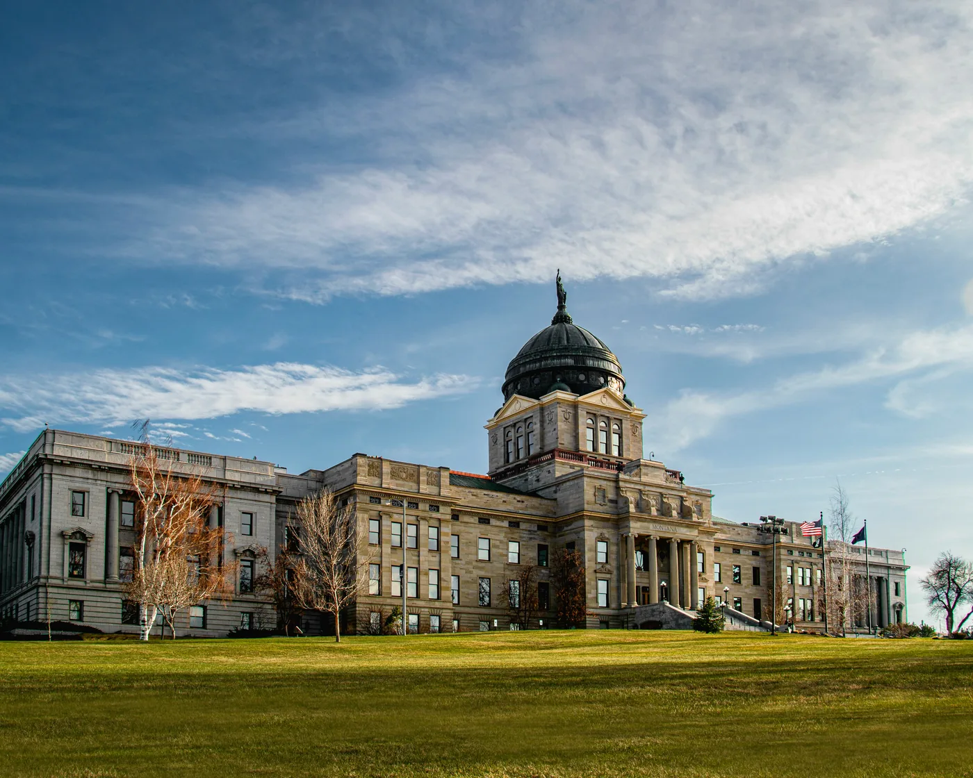 The Montana State Capitol in Helena, with its copper dome, above a green lawn in afternoon light.