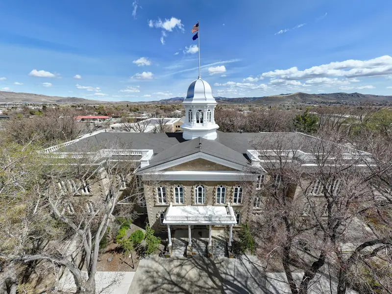 The Nevada State Capitol in Carson City from above, its silver cupola among spring trees, with the Carson Range foothills behind.