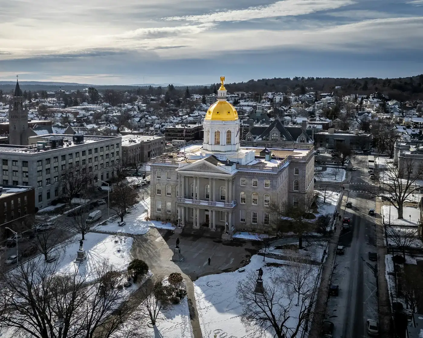 The gold-domed New Hampshire State House in Concord, seen from above on a bright winter afternoon with snow on the grounds.