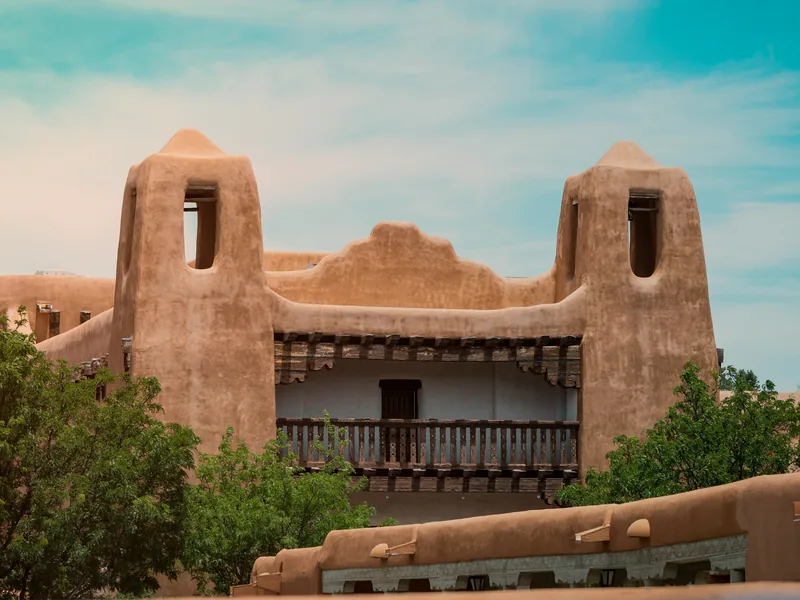 The Pueblo Revival towers and balcony of the New Mexico Museum of Art in Santa Fe under a summer sky.