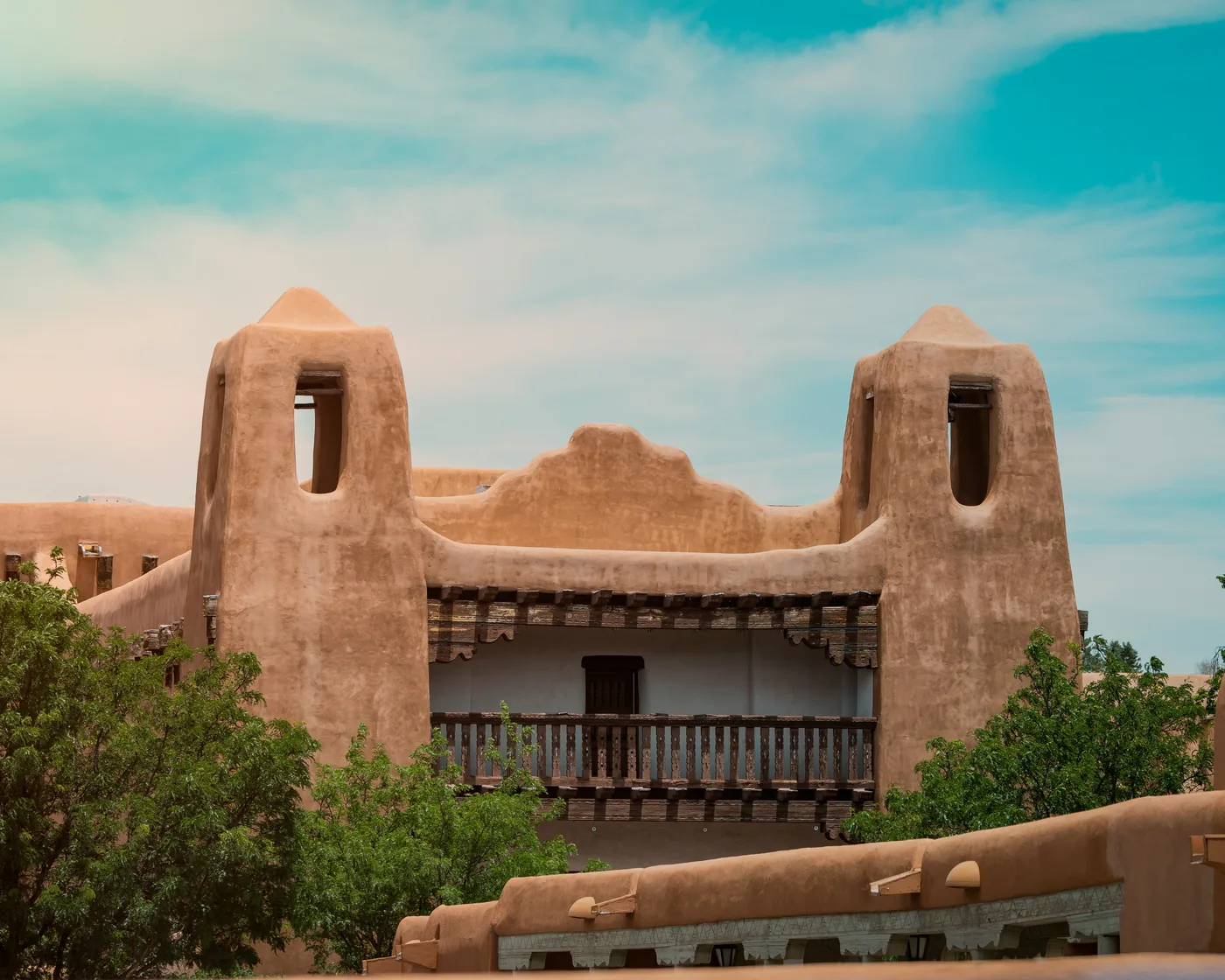 The Pueblo Revival towers and balcony of the New Mexico Museum of Art in Santa Fe under a summer sky.
