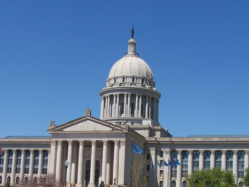 The Oklahoma State Capitol in Oklahoma City, its domed center and long colonnade under a clear blue sky.