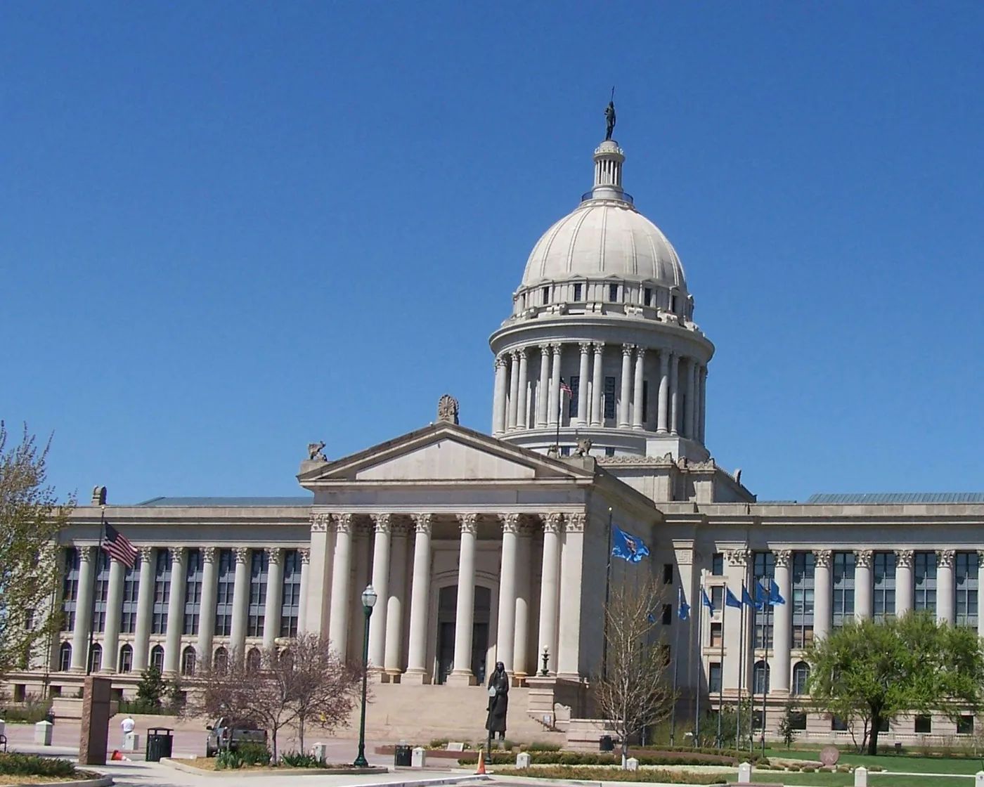 The Oklahoma State Capitol in Oklahoma City, its domed center and long colonnade under a clear blue sky.