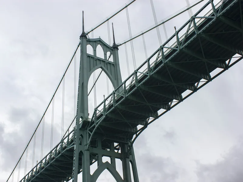A green Gothic tower of the St. Johns Bridge in Portland, seen from below against a cloudy sky.