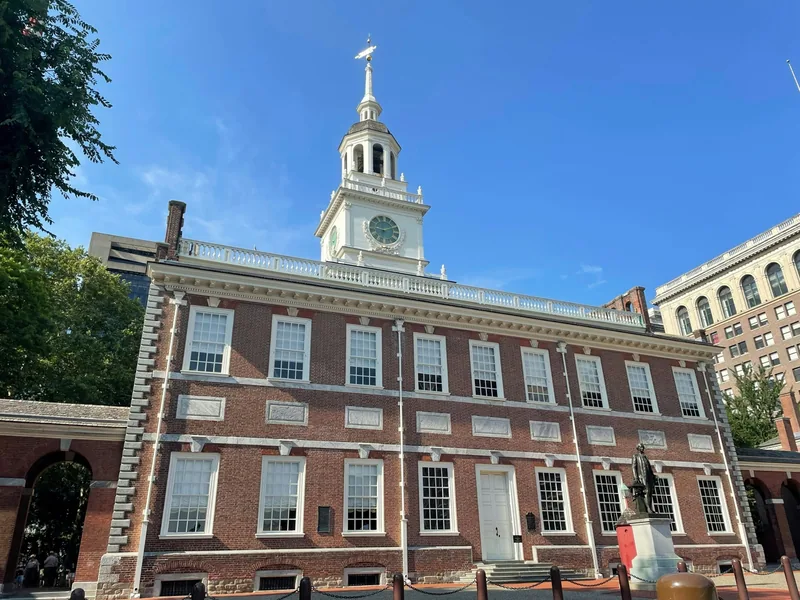 Independence Hall in Philadelphia, its red-brick front and white clock tower under a clear blue sky.
