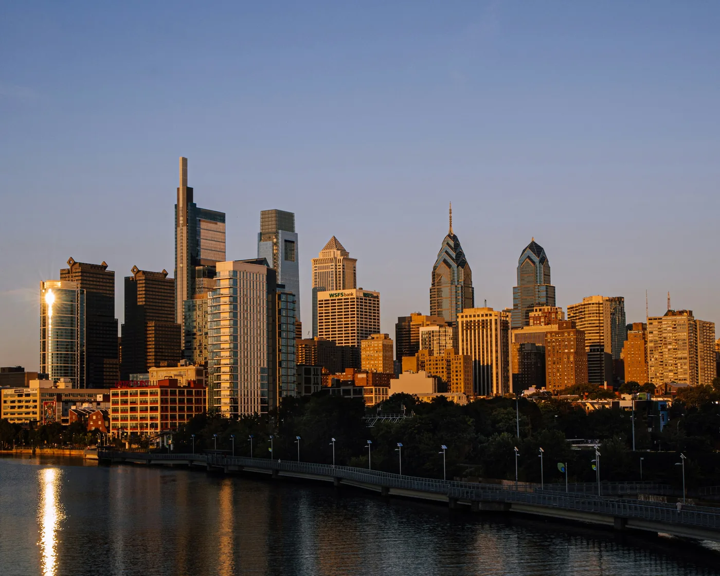 Center City Philadelphia’s skyline in golden-hour light above the Schuylkill River and the Schuylkill River Trail boardwalk.