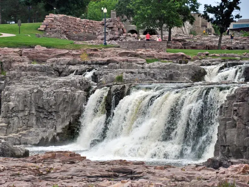 The falls of the Big Sioux River tumbling over pink quartzite at Falls Park in Sioux Falls, with the park lawns above.