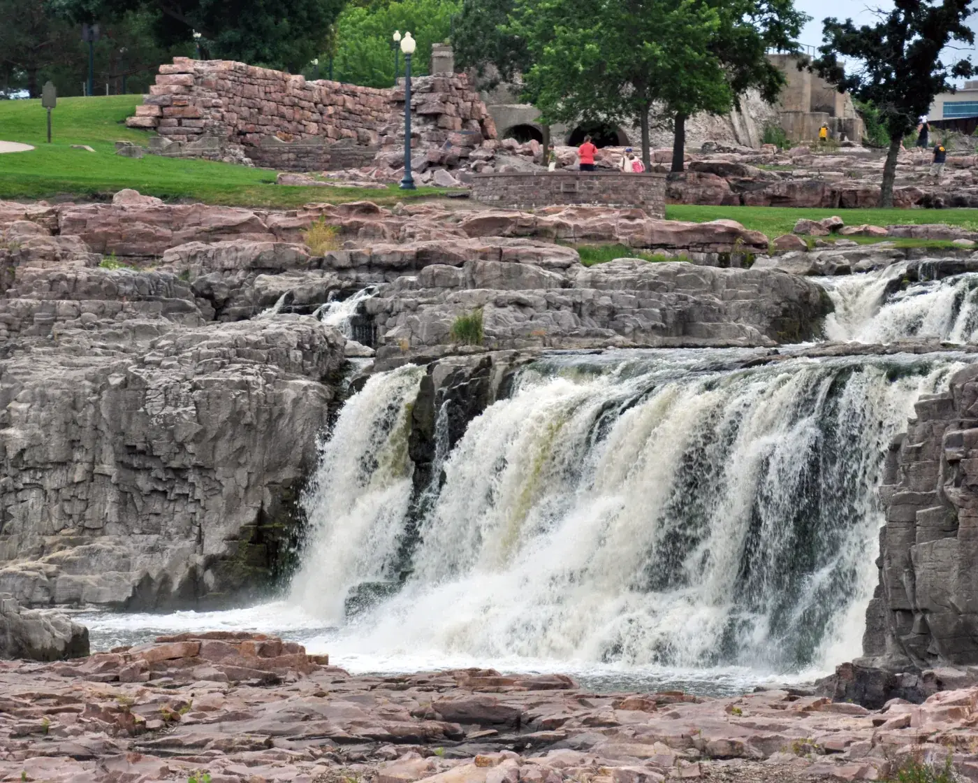 The falls of the Big Sioux River tumbling over pink quartzite at Falls Park in Sioux Falls, with the park lawns above.