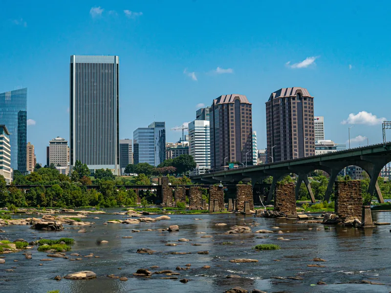 Downtown Richmond’s skyline on a clear summer day above the rocks of the James River and a row of old stone bridge piers.