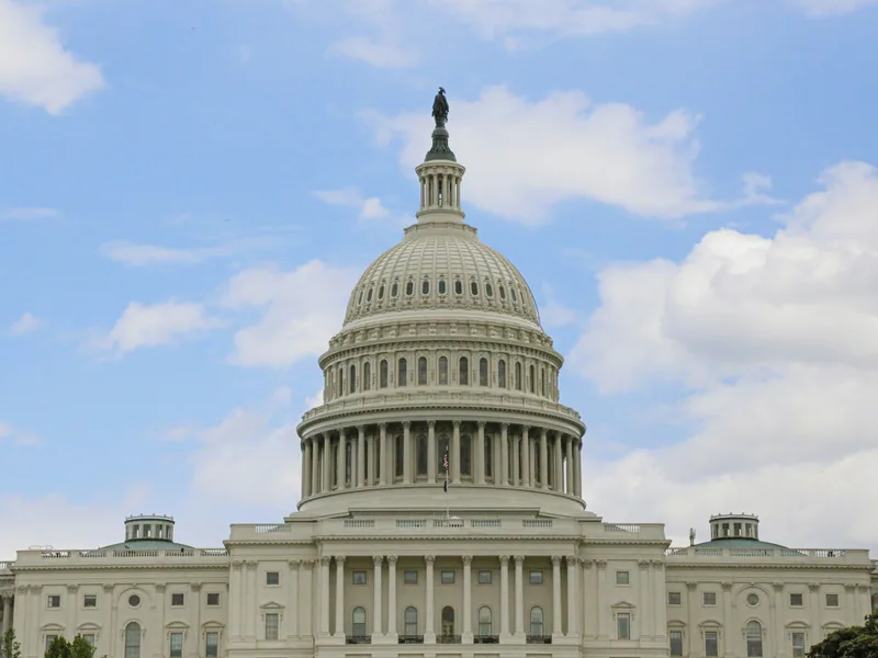 The dome of the US Capitol against a blue sky with white clouds.