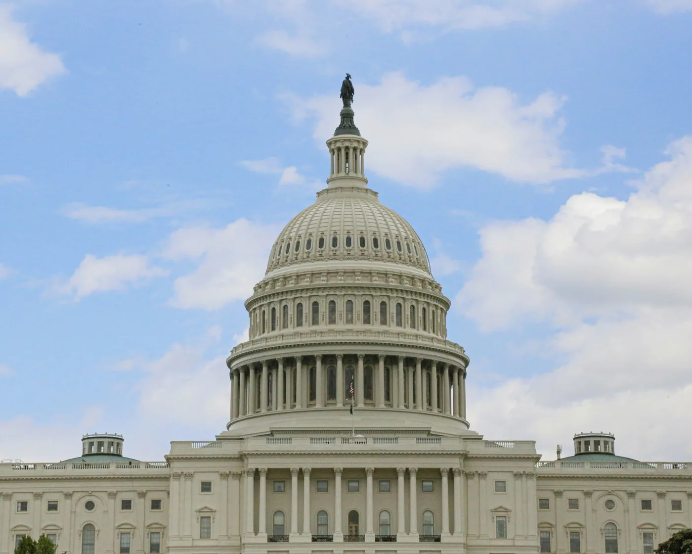 The dome of the US Capitol against a blue sky with white clouds.